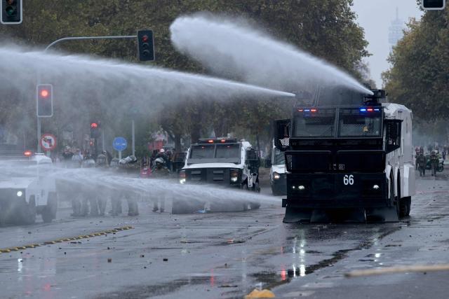 A riot police water cannon truck sprays water at demonstrators during a march organized by unions and social organizations on May Day, marking International Workers Day, in Santiago, on May 1, 2026. (Photo by Rodrigo ARANGUA / AFP)