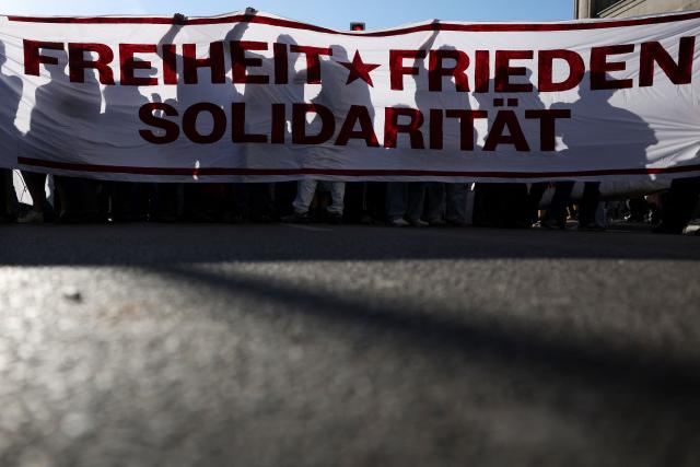 The shadows of participants are seen behind a banner with the lettering 'Freedom, Peace, Solidarity' during the annual leftist May Day demonstration at Oranienplatz Square in Berlin's Kreuzberg district on May 1, 2026. (Photo by Odd ANDERSEN / AFP)