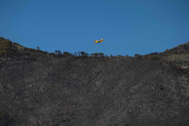 A firefighting plane flies over burnt forest as fireteams tackle a wildfire, in Asciano on May 1, 2026. Italian authorities evacuated some 3,500 people in its famed Tuscany region on May 1, 2026 as they try to tame a wildfire that has been raging for more than 24 hours. Over 800 hectares (nearly 2,000 acres) have been ravaged by the fire in the mountains between the historic cities of Lucca and Pisa. (Photo by Federico SCOPPA / AFP)