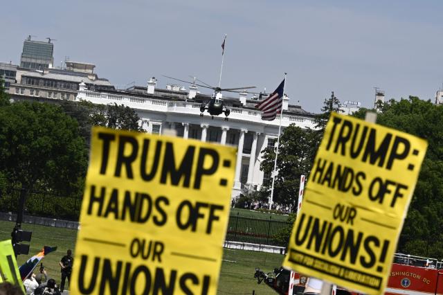 Demonstrators hold signs during a May Day rally marking International Workers' Day as Marine One, with US President DOnald Trump on board, departs from the South Lawn of the White House in Washington, DC, on May 1, 2026. Trump is going to Florida to speak at an event at The Villages and to attend the Forum Club of the Palm Beaches dinner. (Photo by Kent NISHIMURA / AFP)