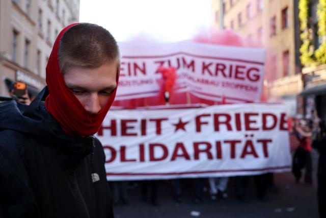 A masked demonstrator looks on as other participants arrive with banners in the background during the annual leftist May Day demonstration in Berlin's Kreuzberg district on May 1, 2026. (Photo by Odd ANDERSEN / AFP)