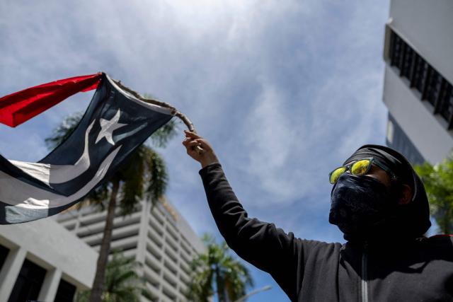 A demonstrator waves a black and white Puerto Rican flag as people take part in a May Day rally marking International Workers' Day in San Juan, Puerto Rico on May 1, 2026. (Photo by Ricardo ARDUENGO / AFP)