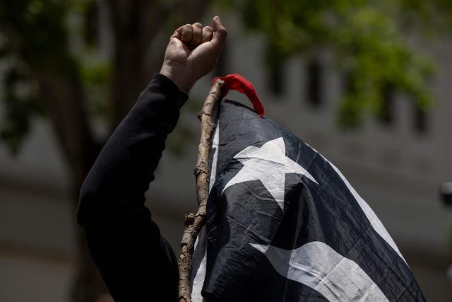 A demonstrator pumps his fist and cover his face with a black and white Puerto Rican flag as people take part in a May Day rally marking International Workers' Day in San Juan, Puerto Rico on May 1, 2026. (Photo by Ricardo ARDUENGO / AFP)