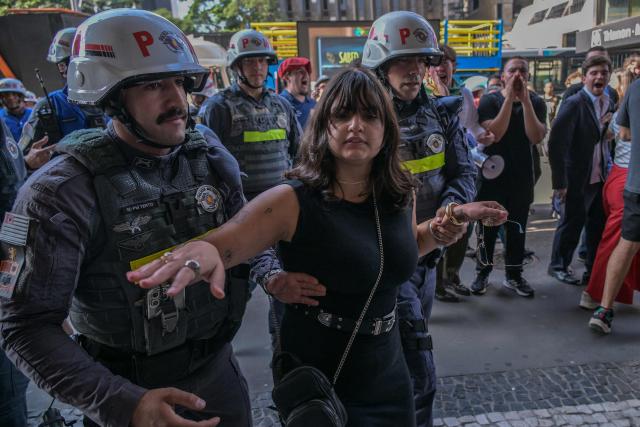 Police escort a left-wing woman away after she confronted supporters of former Brazilian President Jair Bolsonaro (2019-2022) during a demonstration marking International Workers Day, in Sao Paulo, Brazil, on May 1, 2026. (Photo by NELSON ALMEIDA / AFP)