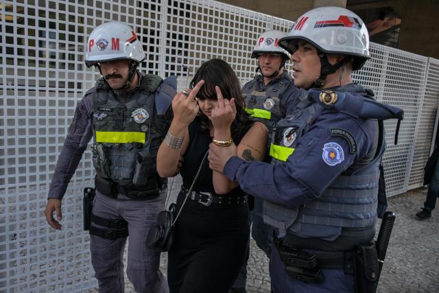 Police escort a left-wing woman away after she confronted supporters of former Brazilian President Jair Bolsonaro (2019-2022) during a demonstration marking International Workers Day, in Sao Paulo, Brazil, on May 1, 2026. (Photo by NELSON ALMEIDA / AFP)