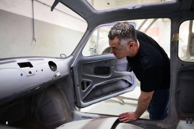 Owner of the Officine Gentile garage, Giovanni Gentile inspects a Fiat 500 model that will be transformed into an electric 500 Jolly Lido model at his workshop in Turin on April 30, 2026. In the Officine Gentile workshop in Turin -- the historic home of Italian carmaker Fiat -- vintage 500 models are getting a makeover with electric engines. The original Fiat 500 became a design icon and some 4.2 million models were made. The retrofitted cars sell for around 40-50,000 euros with convertibles for up to 80,000 euros. (Photo by MARCO BERTORELLO / AFP)