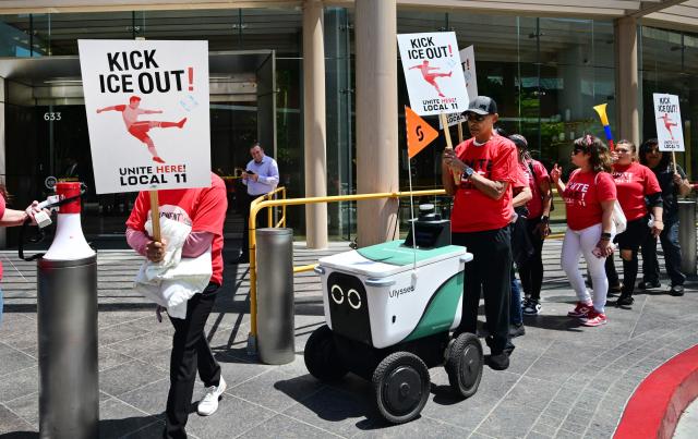 A food delivery robot maneuvers its way past SOFI stadium workers protesting outside FIFA World Cup 26 Los Angeles Office calling for ICE to be banned from the World Cup on May 1, 2026. Eight World Cup matches are planned for SOFI stadium during this summer's World Cup. (Photo by Frederic J. BROWN / AFP)
