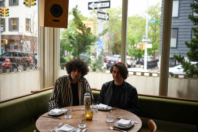Co-founders Siavash Karampour (L) and Sasan Oskouei (R) pose next to a bottle of their brand of the traditional Iranian spirit "Aragh Sagi" at a restaurant in the Brooklyn borough of New York City, on April 28, 2026. Three Iranian men pressed rehydrated raisins at an artisan distillery just outside New York, thousands of miles from their war-struck homeland. They were carefully producing aragh sagi, a traditional spirit banned by the clerical authorities along with all alcohol following the 1979 Islamic revolution. Despite its outlaw moonshine status, the drink is still made clandestinely and consumed inside Iran. (Photo by CHARLY TRIBALLEAU / AFP)