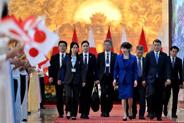 Staff members wave flags to greet Vietnam's Prime Minister Le Minh Hung (2nd R) with Japan's Prime Minister Sanae Takaichi (centre R) at the Government Office in Hanoi on May 2, 2026. (Photo by Nhac NGUYEN / AFP)