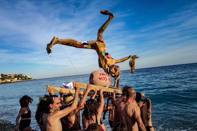 A papier-mache figure is carried to the beachfront as revelers participate at the traditional "Santa Capelina" festival in Nice, south-eastern France, on May 1, 2026. Revelers gather on May 1 in Nice to celebrate the annual Santa Capelina, parading in hand-made hats and sharing a fish soup cooked on site, with each participant contributing their own fish. A Santa figure, built collectively from branches and flowers with a papier-mâché head, is carried in a procession to the beach before casting it into the sea. (Photo by Valery HACHE / AFP)