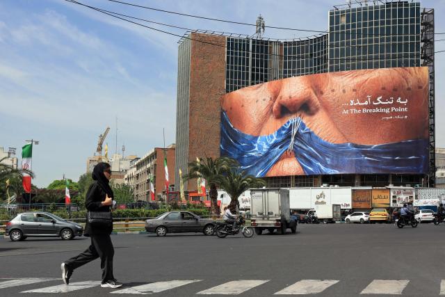 A woman walks past an anti-US billboard referring to President Donald Trump and the Strait of Hormuz, installed on a building at the Valiasr Square in Tehran on May 2, 2026. A senior Iranian military officer said on May 2 that renewed fighting between the US and Iran was "likely", hours after President Donald Trump said he was "not satisfied" with a new Iranian negotiating proposal. (Photo by AFP) / 