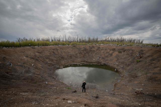 A photographer takes photos of a crater formed by a shelling in 2022 in the village of Dovhenke, Kharkiv region, on May 1, 2026, amid the Russian invasion of Ukraine. (Photo by Ivan SAMOILOV / AFP)