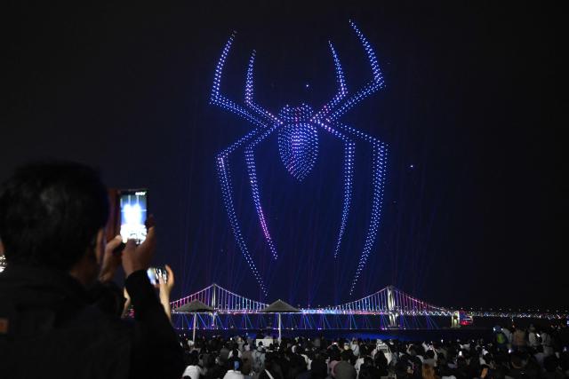 A swarm of 1,500 drones forms the shape of a spider in the night sky above Gwangan Bridge during a drone light show to promote the movie "Spider-Man: Brand New Day" at Gwangalli Beach in Busan on May 2, 2026. (Photo by Jung Yeon-je / AFP)