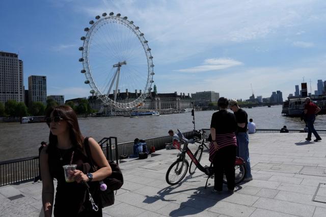 People enjoy the sunshine whilst standing on the banks of the River Thames backdropped by the London Eye in central London on May 2, 2026. (Photo by CARLOS JASSO / AFP)