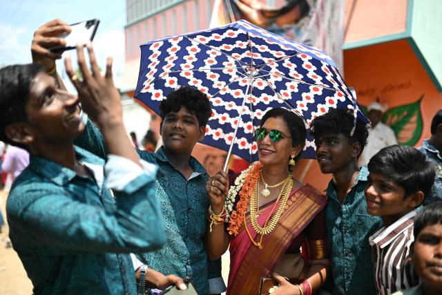 This photograph taken on April 29, 2026 shows Thilothama, a member of the transgender community taking selfies with local boys during the annual Koovagam transgender festival at the Koothandavar temple in Tamil Nadu's Kallakurichi district. For a few fleeting days each year, at the heart of the Koothandavar Temple where ostracised transgender community members from across India come to honour the Hindu deity Aravan, a tradition rooted in millennia-old Hindu texts -- and to enjoy a brief oasis of freedom, for the past 10 years Thilothama has returned to Koovagam, where a beauty pageant and singing contests are held alongside religious rituals. (Photo by R.Satish BABU / AFP)