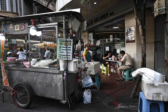 This photo taken on April 29, 2026 shows people eating noodles from a street food cart in Chinatown in Bangkok. Across Bangkok, aromas of garlic, chilli and grilled meat drift from roadside stalls and carts, but tighter controls on vendors threaten livelihoods and the street food culture that defines the Thai capital. (Photo by Lillian SUWANRUMPHA / AFP) / To go with AFP story Thailand-Bangkok-food-culture-economy,FOCUS by Montira Rungjirajittranon
