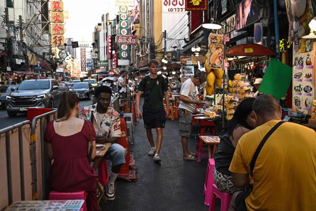This photo taken on April 29, 2026 shows visitors eating local street food in Chinatown in Bangkok. Across Bangkok, aromas of garlic, chilli and grilled meat drift from roadside stalls and carts, but tighter controls on vendors threaten livelihoods and the street food culture that defines the Thai capital. (Photo by Lillian SUWANRUMPHA / AFP) / To go with AFP story Thailand-Bangkok-food-culture-economy,FOCUS by Montira Rungjirajittranon