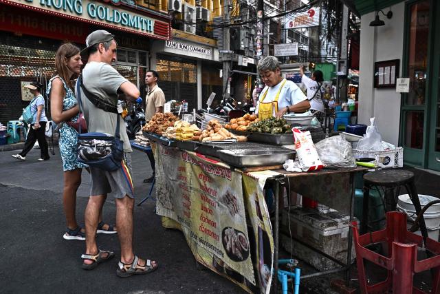 This photo taken on April 29, 2026 shows street food vendor Thitisakulthip Sang-uamsap selling fried vegetarian snacks to visitors in Chinatown in Bangkok. Across Bangkok, aromas of garlic, chilli and grilled meat drift from roadside stalls and carts, but tighter controls on vendors threaten livelihoods and the street food culture that defines the Thai capital. (Photo by Lillian SUWANRUMPHA / AFP) / To go with AFP story Thailand-Bangkok-food-culture-economy,FOCUS by Montira Rungjirajittranon