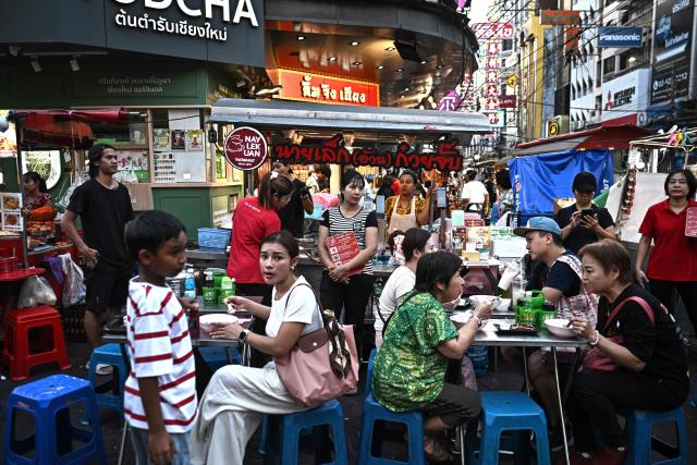 This photo taken on April 29, 2026 shows people eating noodles from a street food stall in Chinatown in Bangkok. Across Bangkok, aromas of garlic, chilli and grilled meat drift from roadside stalls and carts, but tighter controls on vendors threaten livelihoods and the street food culture that defines the Thai capital. (Photo by Lillian SUWANRUMPHA / AFP) / To go with AFP story Thailand-Bangkok-food-culture-economy,FOCUS by Montira Rungjirajittranon