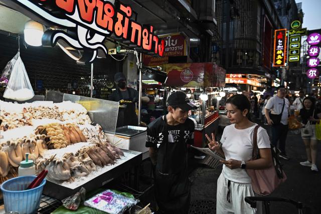 This photo taken on April 29, 2026 shows people ordering grilled seafood from street vendors in Chinatown in Bangkok. Across Bangkok, aromas of garlic, chilli and grilled meat drift from roadside stalls and carts, but tighter controls on vendors threaten livelihoods and the street food culture that defines the Thai capital. (Photo by Lillian SUWANRUMPHA / AFP) / To go with AFP story Thailand-Bangkok-food-culture-economy,FOCUS by Montira Rungjirajittranon