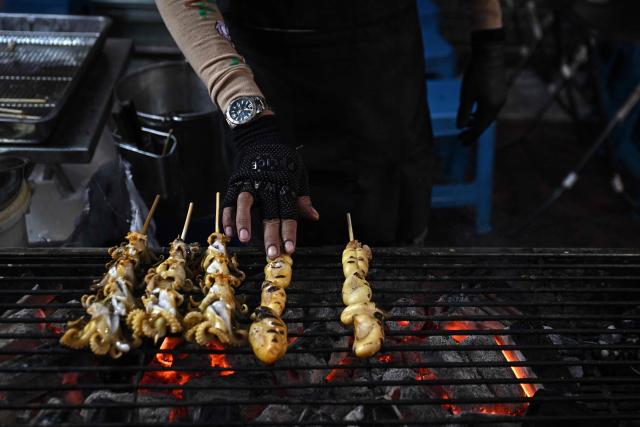 This photo taken on April 29, 2026 shows street food vendors grilling seafood in Chinatown in Bangkok. Across Bangkok, aromas of garlic, chilli and grilled meat drift from roadside stalls and carts, but tighter controls on vendors threaten livelihoods and the street food culture that defines the Thai capital. (Photo by Lillian SUWANRUMPHA / AFP) / To go with AFP story Thailand-Bangkok-food-culture-economy,FOCUS by Montira Rungjirajittranon