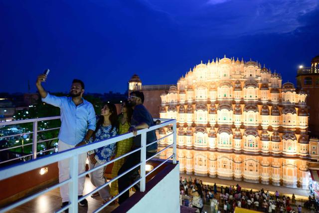 Tourists take a selfie against the backdrop of landmark Hawa Mahal or "Palace of Winds”, at a rooftop cafe in Jaipur on May 2, 2026. (Photo by Manan VATSYAYANA / AFP)