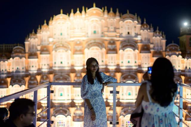A woman poses for photographs against the backdrop of landmark Hawa Mahal or "Palace of Winds”, at a rooftop cafe in Jaipur on May 2, 2026. (Photo by Manan VATSYAYANA / AFP)