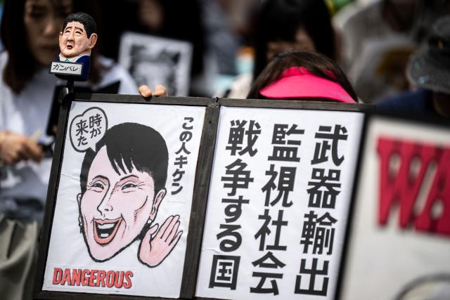 A person holds a toy of Japan's former prime minister Shinzo Abe and a drawing of Japan's Prime Minister Sanae Takaichi and a placard reading "Weapon exports, surveillance society, a country that goes to war", during the Grand Constitution Rally 2026 to mark Constitution Memorial Day in Tokyo on May 3, 2026. (Photo by Philip FONG / AFP)