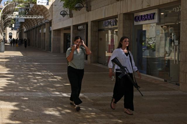 A woman carrying a rifle walks along the Mamila market in Jerusalem on May 3, 2026. (Photo by HAZEM BADER / AFP)