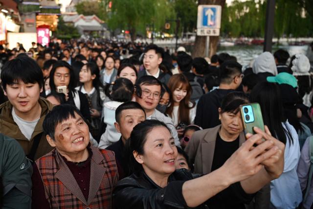 A woman takes a photo at a crowded alley next to Houhai Lake in Beijing on May 3, 2026, the third day of a five-day national May Day holiday. (Photo by GREG BAKER / AFP)