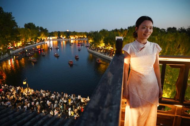 A woman poses for photos on a balcony above Houhai Lake in Beijing on May 3, 2026, the third day of a five-day national May Day holiday. (Photo by GREG BAKER / AFP)