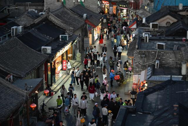 People walk at an alley in a tourist area of Beijing on May 3, 2026, the third day of a five-day national May Day holiday. (Photo by GREG BAKER / AFP)