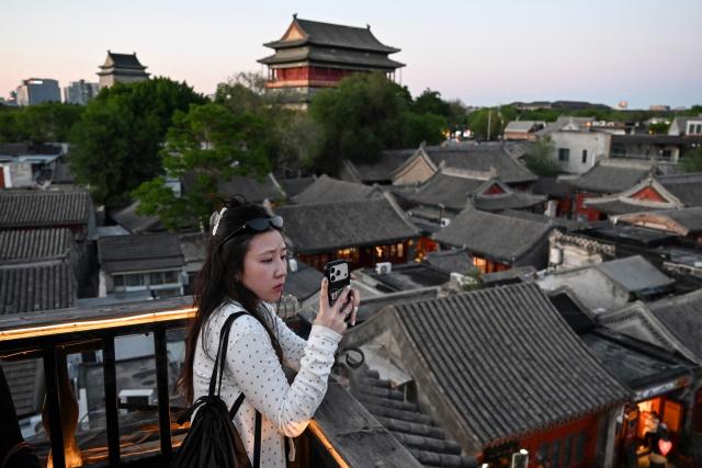 A woman photographs rooftops near the Drum Tower (C) and Bell Tower (L) in Beijing on May 3, 2026 on the third day of a five-day national May Day holiday. (Photo by GREG BAKER / AFP)