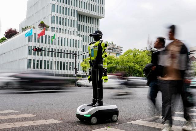 People walk past a humanoid robot police officer in Hangzhou, in China’s eastern Zhejiang province on May 3, 2026 on the third day of a five-day national May Day holiday. The tech hub's traffic police deployed 15 humanoid robots in total to bolster their ranks on May 1. (Photo by Agatha CANTRILL / AFP)
