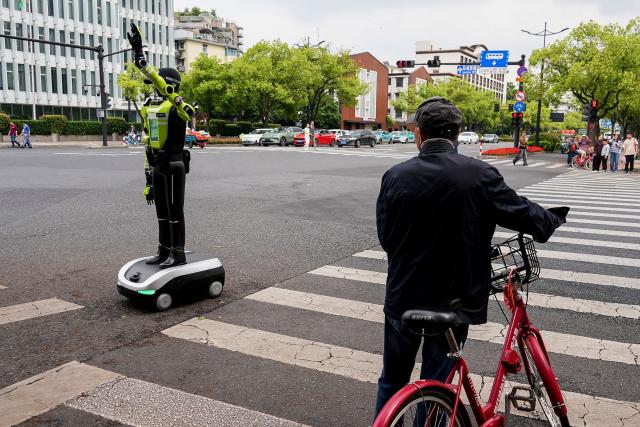 A cyclist looks at a humanoid robot police officer in Hangzhou, in China’s eastern Zhejiang province on May 3, 2026 on the third day of a five-day national May Day holiday. The tech hub's traffic police deployed 15 humanoid robots in total to bolster their ranks on May 1. (Photo by Agatha CANTRILL / AFP)
