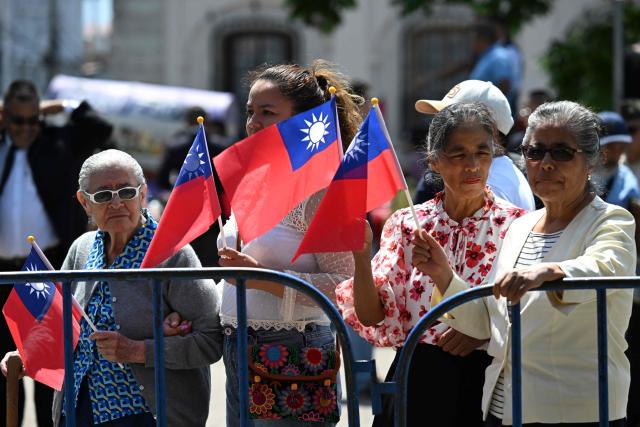 Guatemalans hold Taiwanese flags a navy cadets from a friendship squadron from Taiuwan perform in a music band at Constitution Square in Guatemala City on May 3, 2026. The three vessels -- described as being on a training mission -- powered into Puerto Quetzal, a port town on Guatemala's Pacific coast, in a visit "to strengthen the ties of friendship," Guatemalan officials and Taiwanese diplomats said. (Photo by JOHAN ORDONEZ / AFP)