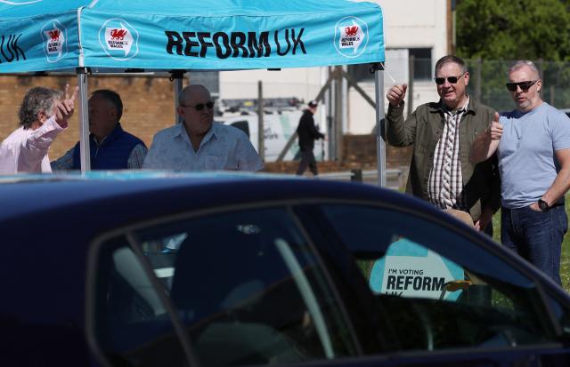Reform UK members gesture towards hooting drivers during campaigning for the Senedd election in Merthyr Tydfil, South Wales on April 24, 2026. Wales -- the cradle of Britain's revered National Health Service and a former industrial powerhouse -- has been a Labour Party stronghold for well over a century. But that is set to end in crunch polls next week as impatient Britons abandon their old political loyalties for anti-establishment parties amid persistent cost of living pressures. (Photo by Darren Staples / AFP) / TO GO WITH AFP STORY by Peter HUTCHISON