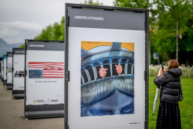 A visitor takes a photo of the exhibition “Dessins pour la libertй” (“Drawings for Freedom”), held to mark World Press Freedom Day on the shores of Lake Geneva in Geneva on May 4, 2026. (Photo by Fabrice COFFRINI / AFP)