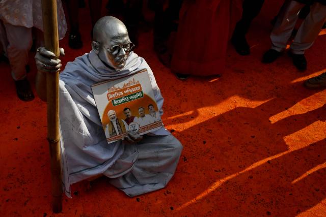A Bharatiya Janata Party (BJP) supporter dressed as Mahatma Gandhi sits along a street smeared in saffron colour to celebrate during vote counting for the West Bengal Legislative Assembly elections, near the party head office in Kolkata on May 4, 2026. Vote counting in key Indian state elections was underway on May 4 under tight security, with the focus on West Bengal, where Prime Minister Narendra Modi's party appeared set for victory. (Photo by Dibyangshu SARKAR / AFP)