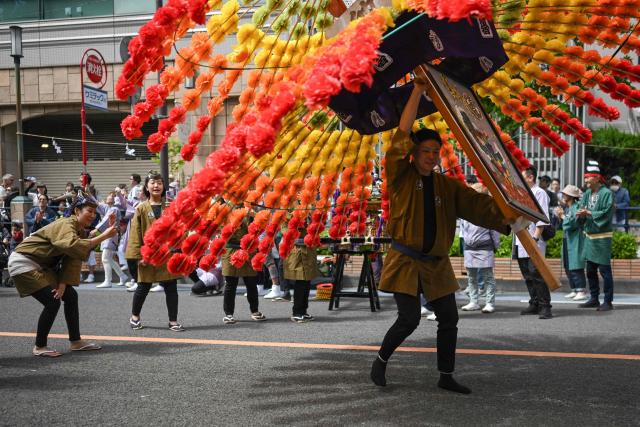 A festival participant spins an elaborate three-meter-tall decorated lantern tower known as Mant? through the streets of Fuchu during the Kurayami Matsuri, or "Festival of Darkness," at Okunitama Shrine in western Tokyo on May 4, 2026, as neighbourhood groups compete in an ancient tradition to keep their 50-kilogram towers twirling the longest while judges assess the artistry of each team's decorated pole. (Photo by Andrew CABALLERO-REYNOLDS / AFP)
