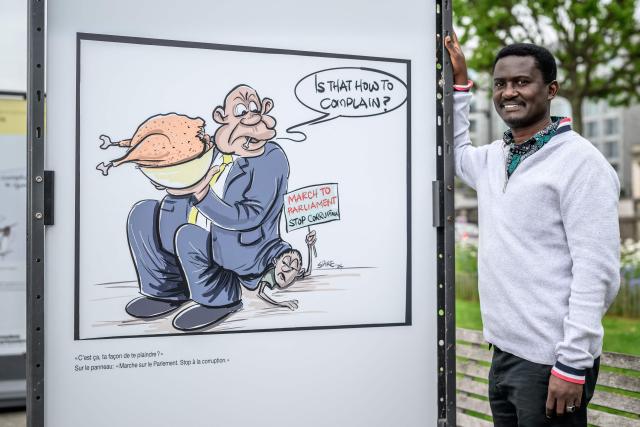 Laureate of the Kofi Annan Courage in Cartooning Award, Ugandan columnist, editorial cartoonist and author Jimmy Spire Ssentongo poses next to one of his cartoons as part of the exhibition titled “Dessins pour la liberte” (“Drawings for Freedom”), held to mark World Press Freedom Day, on the shores of Lake Geneva in Geneva, on May 4, 2026. (Photo by Fabrice COFFRINI / AFP)