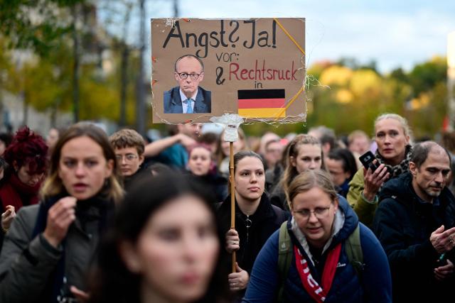(FILES) A participant holds up a placard with the lettering 'Fear? Yes, of a shift to the right in Germany' and a photo of German Chancellor Friedrich Merz next to a German flag during a demonstration with the title 'We Are the Daughters' in front of the Konrad Adenauer Haus, the headquarters of Merz' Christian Democratic Union (CDU), in Berlin on October 21, 2025. German lawmakers on May 6, 2025 elected conservative Friedrich Merz as chancellor in a second-round vote, a victory marred by his surprise defeat in an initial ballot. A year after German Chancellor Friedrich Merz took office vowing to revive the political centre, the far-right AfD party has risen to the top of the polls while Merz's coalition faces miserable approval numbers. (Photo by John MACDOUGALL / AFP)