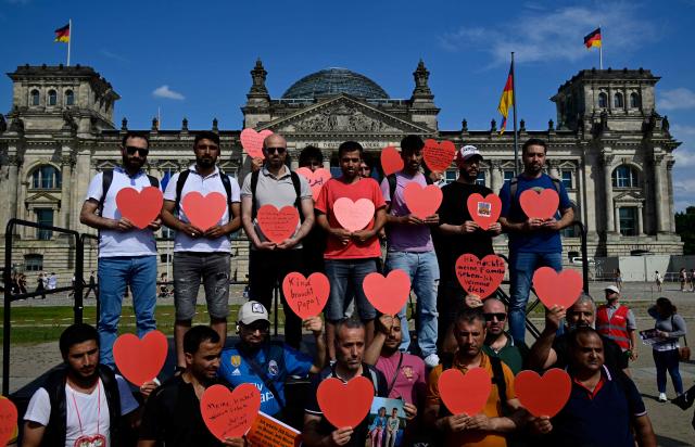 (FILES) Demonstrators hold heart-shaped posters as they protest in front of the Reichstag building that houses the Bundestag (lower house of parliament) against the German government's migration policy, on June 26, 2025 in Berlin. A year ago, German lawmakers elected conservative Friedrich Merz as chancellor. He took office vowing to revive the political centre, but the far-right AfD party has risen to the top of the polls while Merz's coalition faces miserable approval numbers. The chancellor had vowed to diminish the AfD's appeal with two main strategies -- taking a tough stance on immigration to outflank the far-right party on the issue, and aiming to enact bold reforms to prove that centrist parties are still capable of acting. (Photo by John MACDOUGALL / AFP)