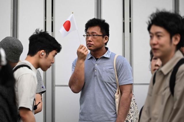 A man waves Japan's national flag as others walk past on the street near a nationalist rally near Ikebukuro Station in Tokyo's Toshima district on May 4, 2026, where participants called for stricter immigration controls and denounced the Japan Communist Party. (Photo by Andrew CABALLERO-REYNOLDS / AFP)