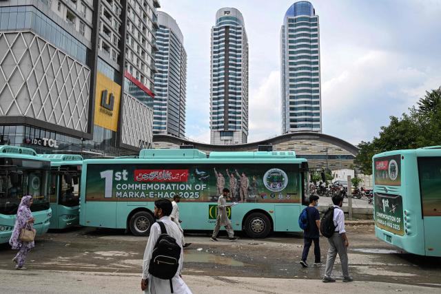 Commuters walk past a government passenger bus carrying a poster of Pakistan's Army Chief and Field Marshal Syed Asim Munir (L) in Islamabad on May 4, 2026 commemorating one year of India-Pakistan clashes after an attack in Indian-administered Kashmir. (Photo by Aamir QURESHI / AFP)