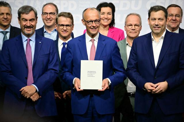 (FILES) The leader of Germany's conservative Christian Democratic Union (CDU) party Friedrich Merz (C), the co-chairman of Germany's Social Democratic Party (SPD) Lars Klingbeil (C-R) and the leader of Bavaria's conservative Christian Social Union (CSU) party Markus Soeder (C-L) pose with members of the new cabinet and party officials after signing a coalition deal to form the country's new government, on May 5, 2025 in Berlin. A year ago, German lawmakers elected conservative Friedrich Merz as chancellor. The chancellor had vowed to diminish the appeal of the country's far-right AfD party with two main strategies -- taking a tough stance on immigration to outflank the far-right party on the issue, and aiming to enact bold reforms to prove that centrist parties are still capable of acting. Tighter immigration rules have led to a significant decrease in arrivals -- but the chancellor does not appear to be benefitting political. Meanwhile the reform drive has stalled due to bickering between the conservative CDU and the social democratic SPD coalition parties, with the long-struggling economy making a slower than expected recovery. (Photo by Tobias SCHWARZ / AFP)