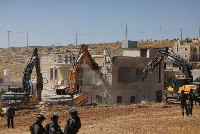 Israeli security forces stand guard as excavators demolish a Palestinian house that was built without a permit, in the village of al-Dirat near Yatta town in the occupied West Bank city of Hebron, on May 4, 2026. The occupied West Bank has been gripped by almost daily violence since the start of the Gaza war in October 2023, involving both Israeli troops and settlers. (Photo by HAZEM BADER / AFP)
