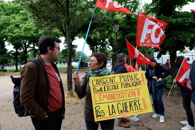 A demonstrator holds a placard reading "Public money for public school, not for war" during a rally in front of the National Assembly to protest against the military spending bill, in Paris on May 4, 2026. (Photo by Xavier GALIANA / AFP)