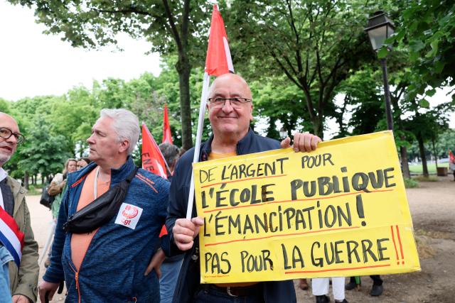 A demonstrator holds a placard reading "Public money for public school, not war" during a rally in front of the National Assembly to protest against the military spending bill, in Paris on May 4, 2026. (Photo by Xavier GALIANA / AFP)