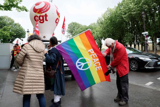 A demonstrator holds a peace rainbow flag during a rally in front of the National Assembly to protest against the military spending bill, in Paris on May 4, 2026. (Photo by Xavier GALIANA / AFP)